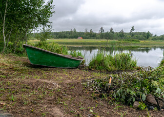 lake shore and boat, calm lake water surface, tree reflections, cloudy day, fishing concept