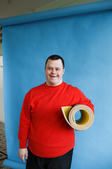 a man with down syndrome in a red sweater stands on a blue background.