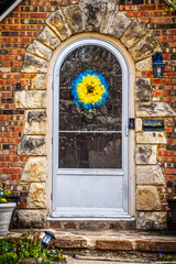 Fototapeta na wymiar Cute rock framed door in brick house with arched storm door and blue and yellow wreath in support of Ukraine