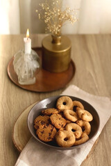 Bowl of sugar cookies and chocolate chip cookies, lit candle and vase with flowers on the table. Selective focus.