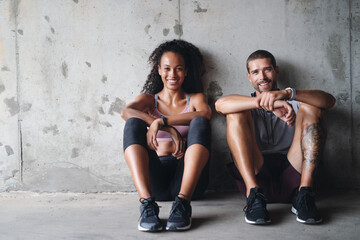 Were down but not out. Portrait of a sporty young couple sitting down against a wall while exercising inside a parking lot. - Powered by Adobe