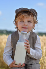 A blond boy in the field with a bottle of milk