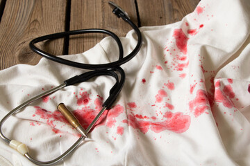 A stethoscope and a bullet lie on a dress with red blood stains, traces of blood on things and a...