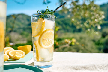Summer refreshing lemonade drink or alcoholic cocktail with ice, rosemary and lemon slices on the...