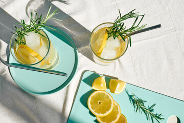 Summer refreshing lemonade drink or alcoholic cocktail with ice, rosemary and lemon slices on the...