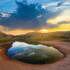 small puddle among sandy prairie at the dramatic sunset