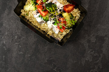 Healthy bowl with bulgur, broccoli, chicken in cream sauce, greens and tomatoes isolated on dark background. Healthy food delivery service and daily ration concept. Free space for text.