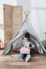 full length view of girl sitting on floor in wigwam and opening gift box. © LIGHTFIELD STUDIOS