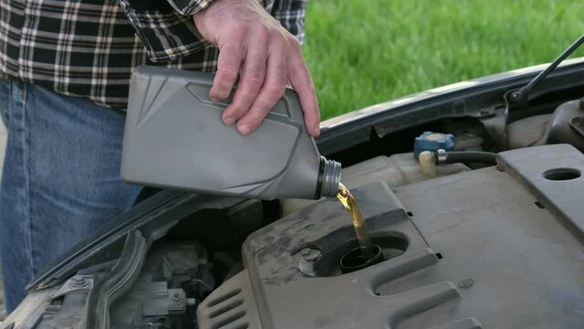 Driver or worker pouring fresh oil to car engine
