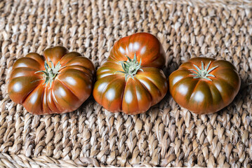 Three tomatoes of the black Raf variety, with different shapes on a rustic background.