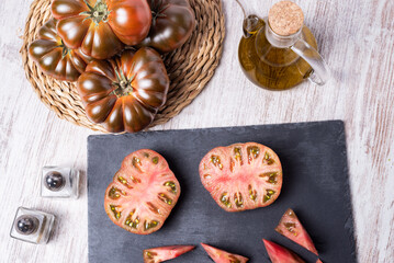 Raf tomato of the black variety (Othello) chopped and another open in two parts, on a rustic stone plate, overhead view.