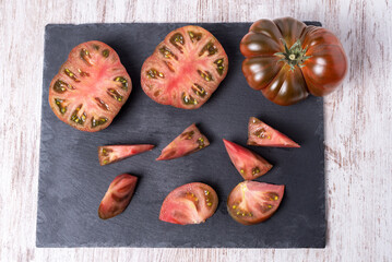 Raf tomato of the black variety (Othello) chopped and another open in two parts, on a rustic stone plate, overhead view.