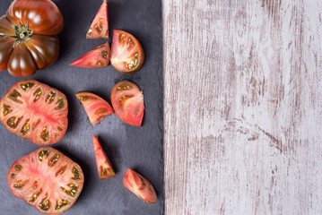 Raf tomato of the black variety, one chopped and the other open in two parts, on a stone plate, on a rustic white table.