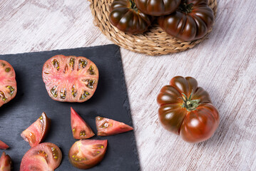 Raf tomato of the black variety, one chopped and the other open in two parts, on a stone plate, on a rustic white table, accompanied by olive oil. Aerial view.