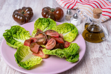 Lettuce and raf tomato salad without seasoning, next to an oil can, salt and pepper.