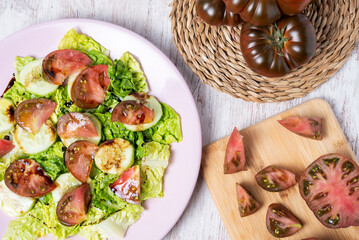 Lettuce, cucumber and raf tomato salad, dressed with olive oil, salt and balsamic vinegar, next to a cutting board with an open and chopped tomato.