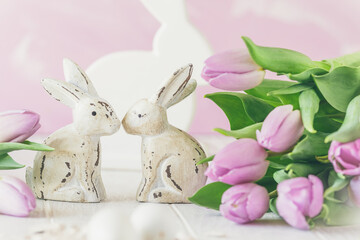 Two white wooden Easter bunnies surrounded by fresh pink tulips