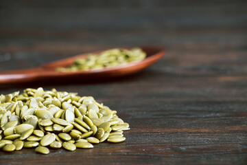 Pumpkin seeds in a wooden spoon on a wooden background. Healthy food. Scattered seeds of pumpkin. Copy space