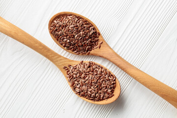 Wooden spoons with flaxseed on a white wooden table.