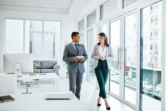 A Wireless Equipped Workforce Keeps Business Moving Forward. Shot Of A Young Businessman And Businesswoman Having A Discussion While Waking Through A Modern Office.