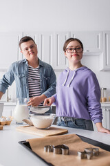 Teenagers in down syndrome looking at camera near food in kitchen.