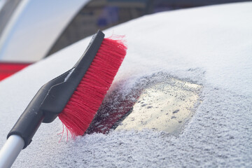 To clean snow with a brush from the windshield of a car after a snowfall in winter