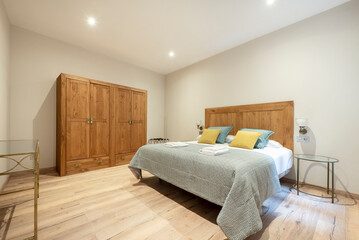 Double bed with light wood headboard with four-door wardrobe, chestnut wood flooring and glass and metal nightstands
