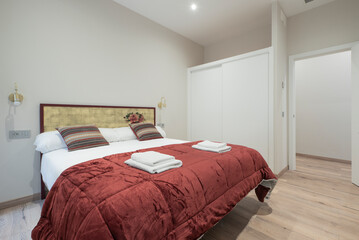 Double bed with red duvet, matching cushions, wooden headboard and built-in wardrobe with white...
