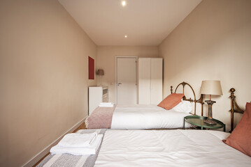 Bedroom with separate beds with brass headboards, white wardrobe and matching chest of drawers
