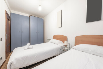 Bedroom with twin beds with light wood headboards with white duvets, and twin gray cabinets