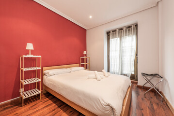 Bedroom with oak wood double bed, twin bookcases on either side of the bed, red painted walls and reddish wood floor and balcony with white curtains