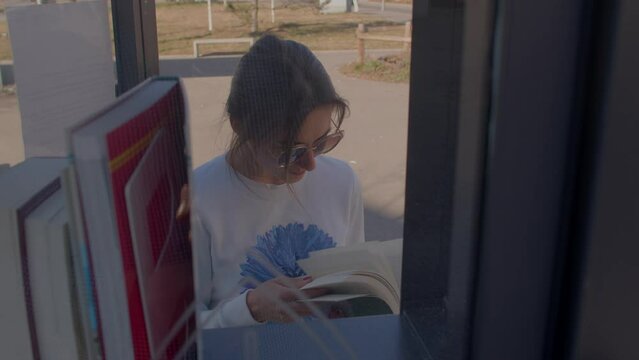 Teenage girl leafs through a book while traveling. Ways of replenishment of the vocabulary. Free public library books sharing box. 