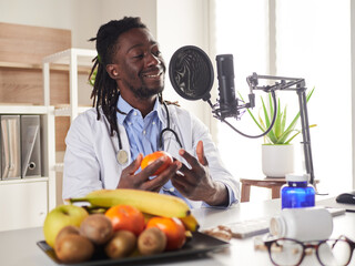 Afroamerican nutritionist looking at camera and showing healthy fruits in the consultation recording video blog