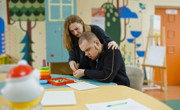 A female psychologist works with an adult boy with autism in the office.