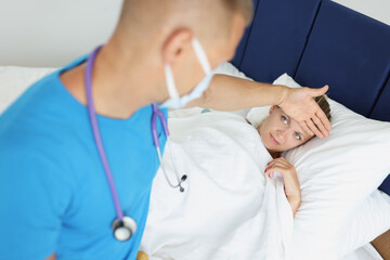 Doctor touches forehead of sick woman in bed