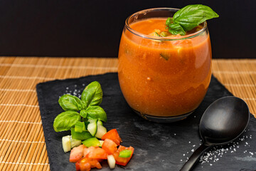 Important Glass with the refreshing Andalusian Gazpacho on a black slab on a mat. A cold vegetable and organic soup or drink that is drunk in summer or hot days. Lower view.