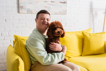 Happy teenager with down syndrome hugging poodle on couch.