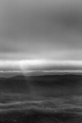 Sun rays coming down from some clouds over a valley filled by fog, illuminating part of it