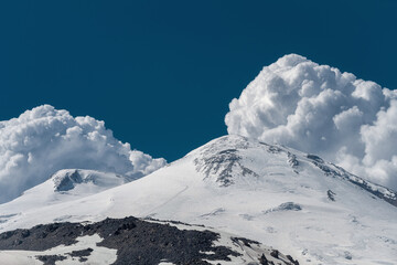 Fototapeta na wymiar The top of Mount Elbrus. White and blue landscape. Elbrus volcano. Snowy peak in summer. Beautiful lush clouds over the mountain.