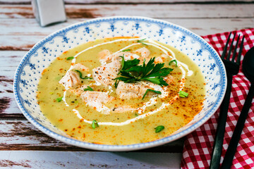 Exquisite dish with a homemade cream of poultry soup with chicken pieces, parsley and cream on a rustic or country style wooden table. Natural and simple food concept. High view