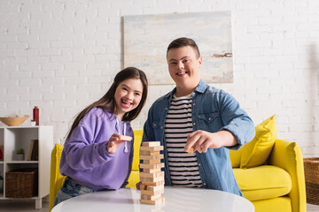 Happy friends with down syndrome looking at camera near wood blocks game at home.