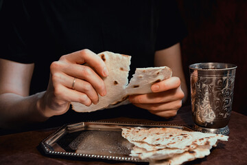 Female hands break a cake for the Easter rite of communion in a church on a silver platter next to...
