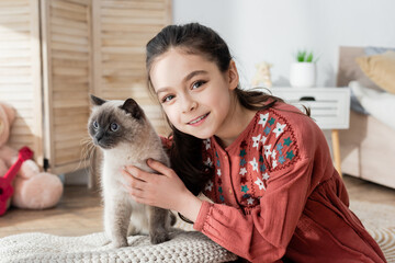 cheerful preteen girl hugging fluffy cat and looking at camera.