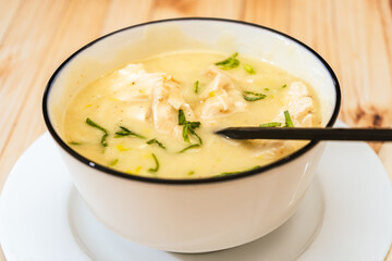 Modern bowl with a traditional homemade cream of poultry soup with chicken pieces, parsley and cream on a rustic or country style wooden table. Natural and simple food concept.