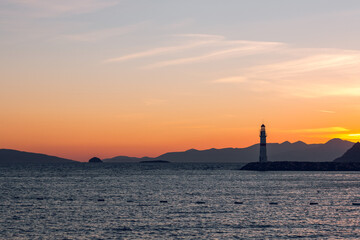 Fototapeta premium Seascape at sunshine. Lighthouse and sailings on the coast. Turgutreis Lighthouse at Sunset. Sea breeze and salty fresh smell.