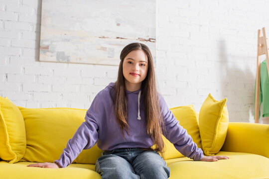 Smiling teenage girl with down syndrome sitting on couch at home.