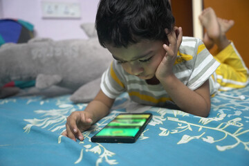 a toddler baby boy engaged in watching and exploring mobile phone.Screen time addiction concept...