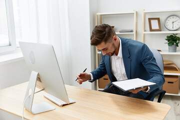 handsome businessman writes in documents at the desk in the office Gray background