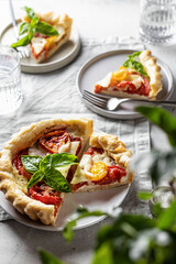 Summer puff pastry tart with tomato, mozzarella and Bazil, composition with greenery in blur