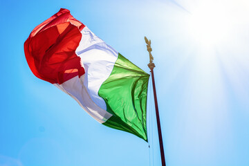waving flag of Italy against a blue sky with sun, italian background national public holiday